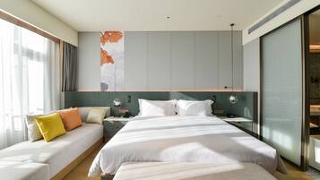 A modern hotel room with a large bed, a sofa bed, a bedside table, and a large window.