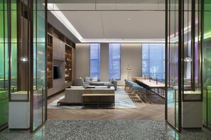 Una sala de estar moderna con sofá, mesa de centro y televisor, ventanas amplias y vista a la ciudad.