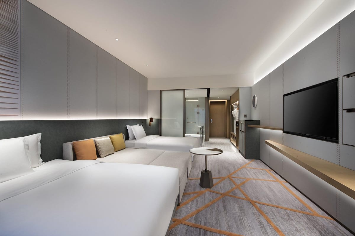 Una habitación de hotel moderna con dos camas, un televisor, una mesita pequeña y una alfombra con diseños geométricos.