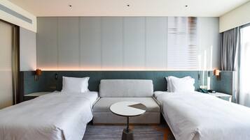 A hotel room with two beds, a sofa, a small round table, and a large window with curtains.