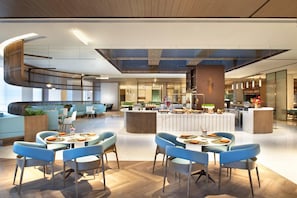 Een moderne hotellobby met een centraal zitgedeelte, een trap en een receptiebalie.