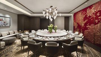 A modern dining room with a round table, chairs, a chandelier, and a red decorative wall.