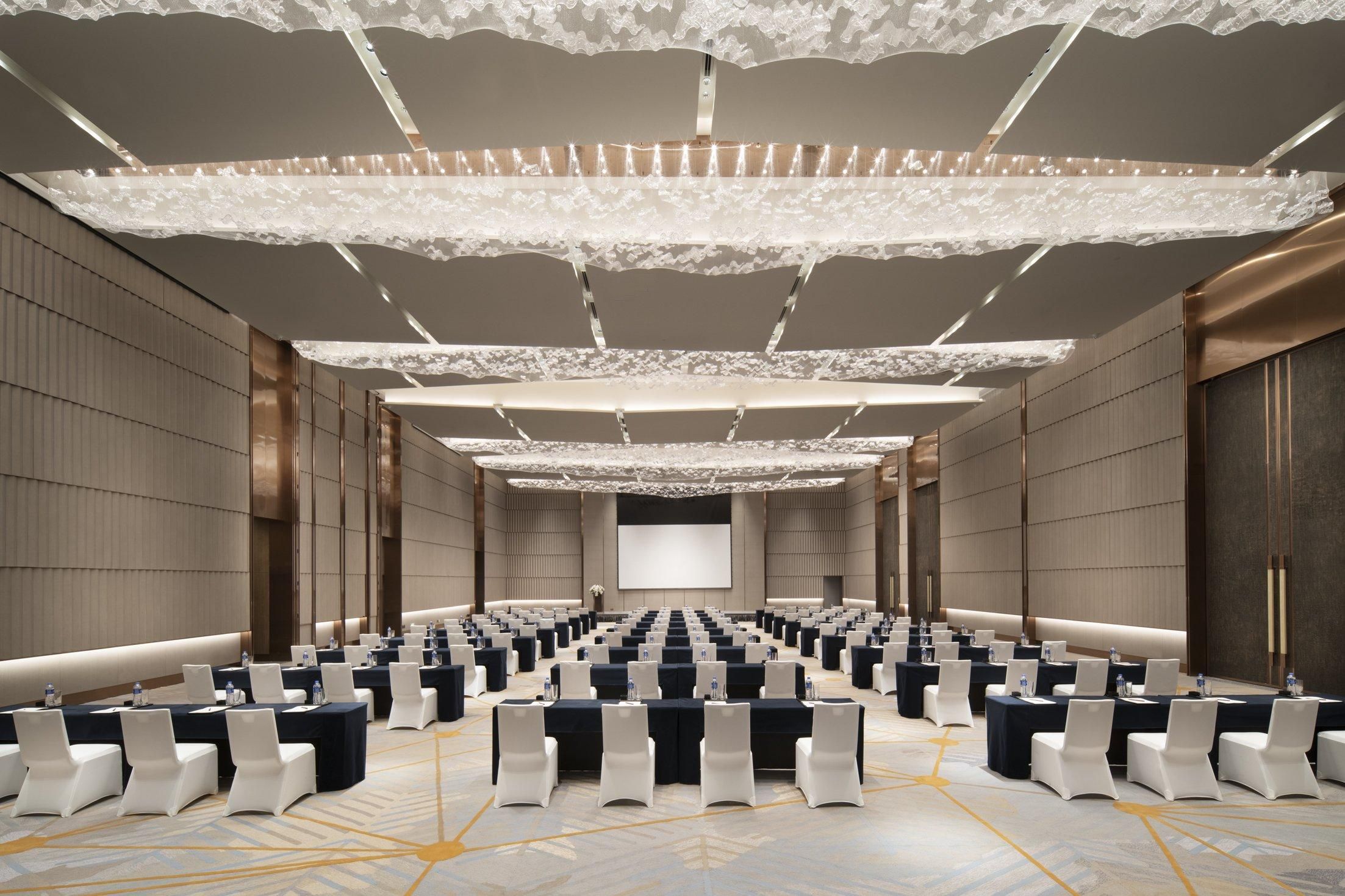 A conference room with rows of tables and chairs, a large screen at the front, and a decorative ceiling.