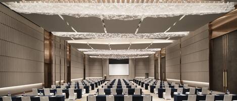 A conference room with rows of tables and chairs, a large screen at the front, and a decorative ceiling.