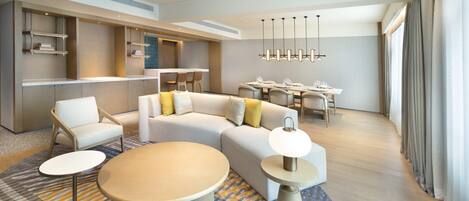 A modern hotel room with a sofa, two round tables, a dining area, and built-in shelves.