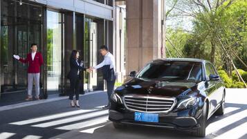 A black car parked in front of a building with glass doors.