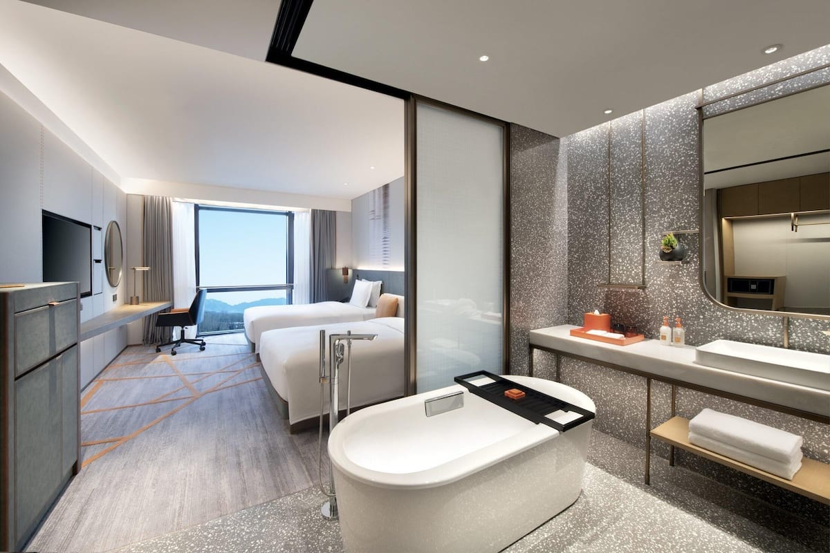 Habitación de hotel moderna con una cama grande, un escritorio independiente, una bañera, un espejo amplio y vistas a las montañas.