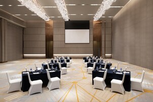 A conference room with a large screen, multiple tables with chairs, and a patterned carpet.