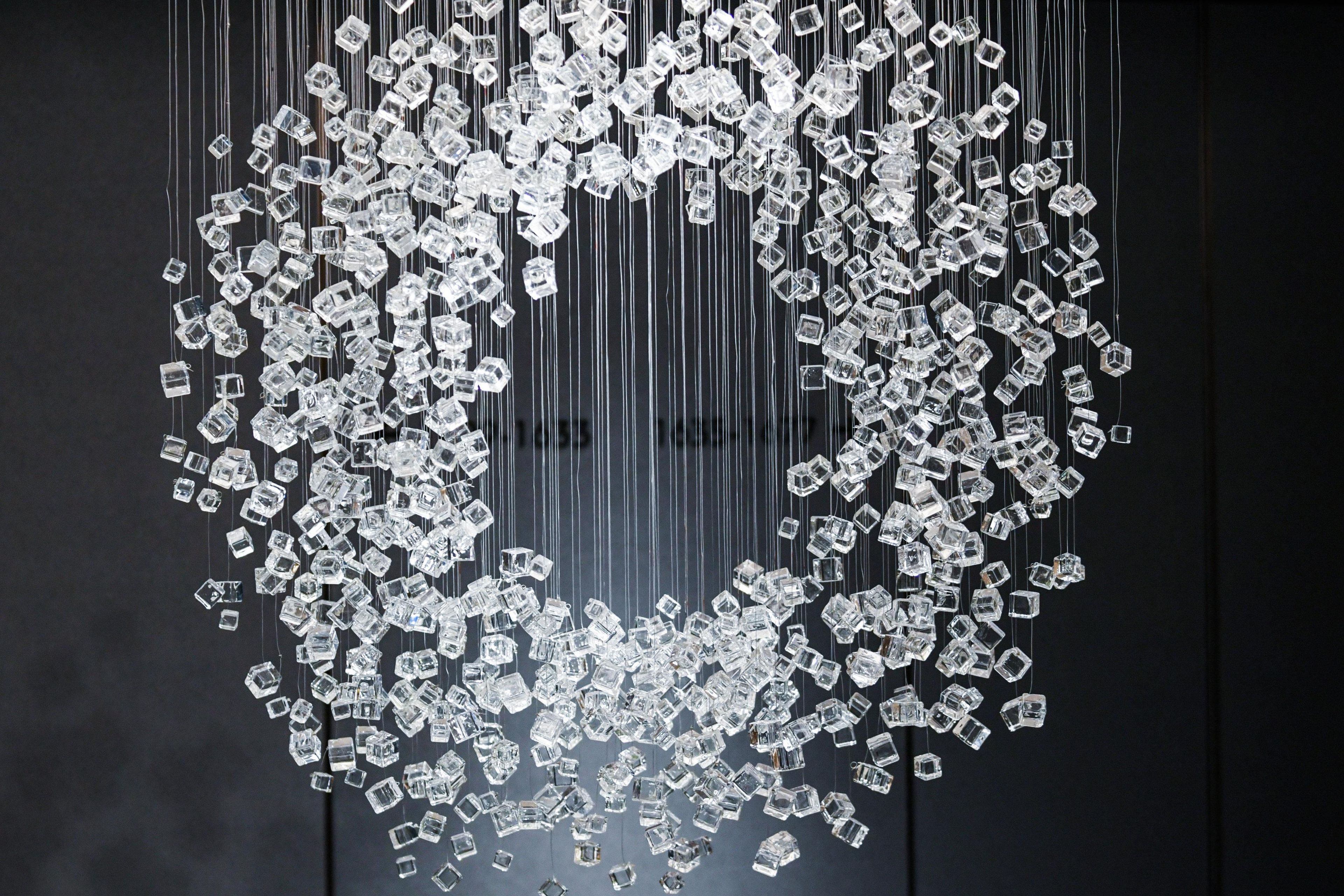 Una instalación geométrica de cubos transparentes suspendidos por hilos sobre un fondo oscuro.