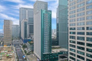 Un edificio de gran altura con fachada de vidrio moderna, rodeado de otros edificios altos y una calle concurrida con obras de construcción visibles.