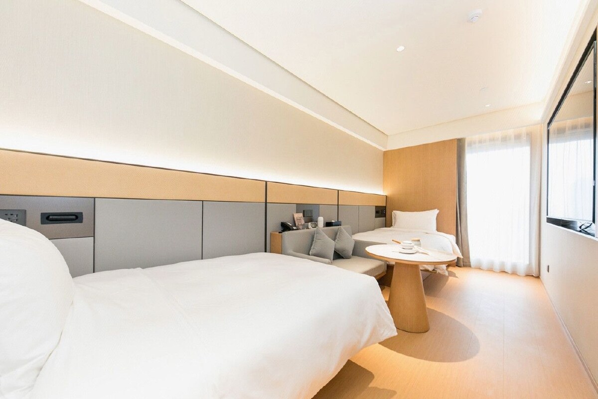 Una habitación de hotel moderna con una cama grande, una mesita pequeña y una consola junto a la cama.