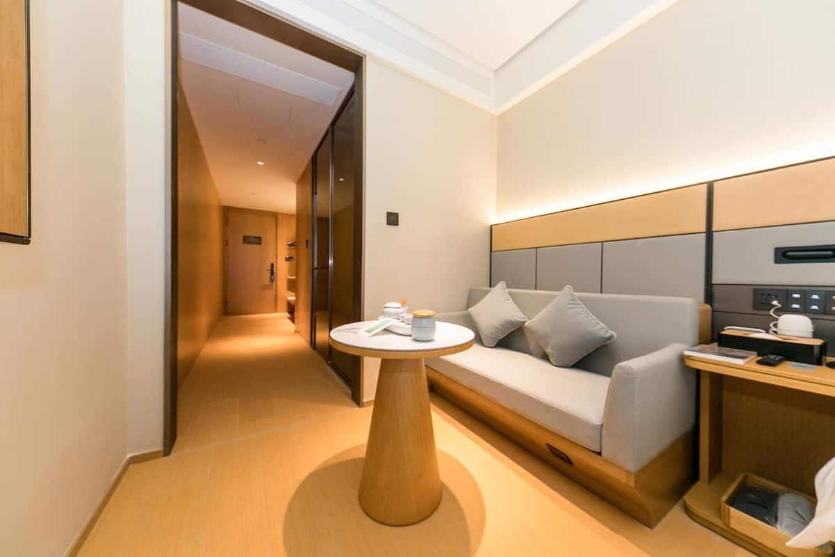 Ein Hotelzimmer mit einer Couch, einem Nachttisch, einer Lampe, einem Spiegel und einem Holzboden.