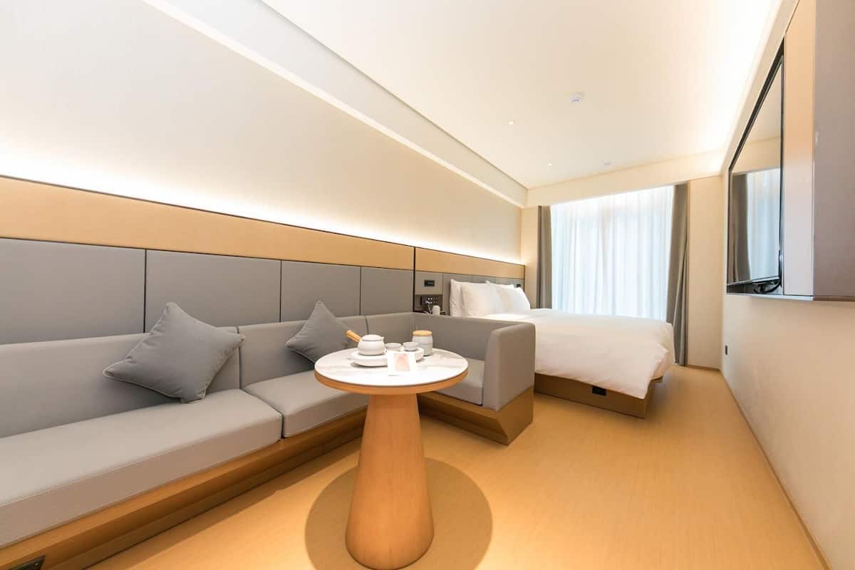 Ein modernes Hotelzimmer mit einer Couch, einem Nachttisch, einem Bett und einem Fernseher.