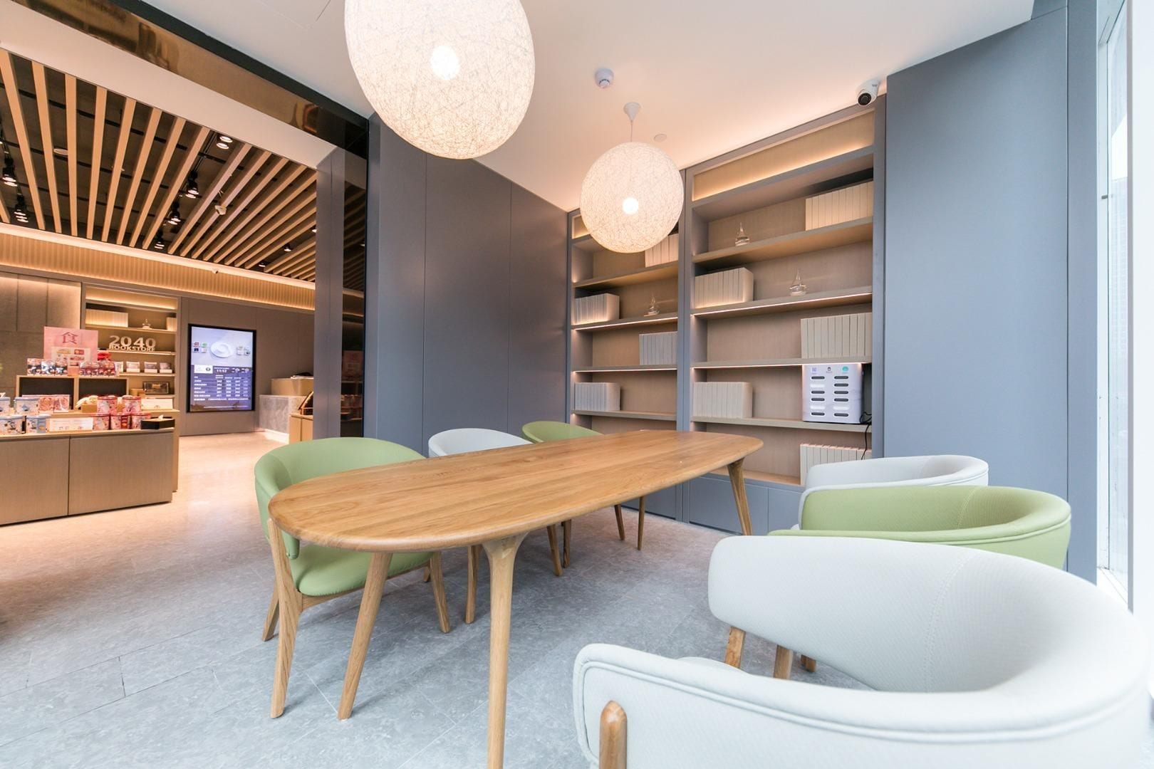 Un interior moderno con una mesa de madera, sillas verdes y blancas, y una estantería.