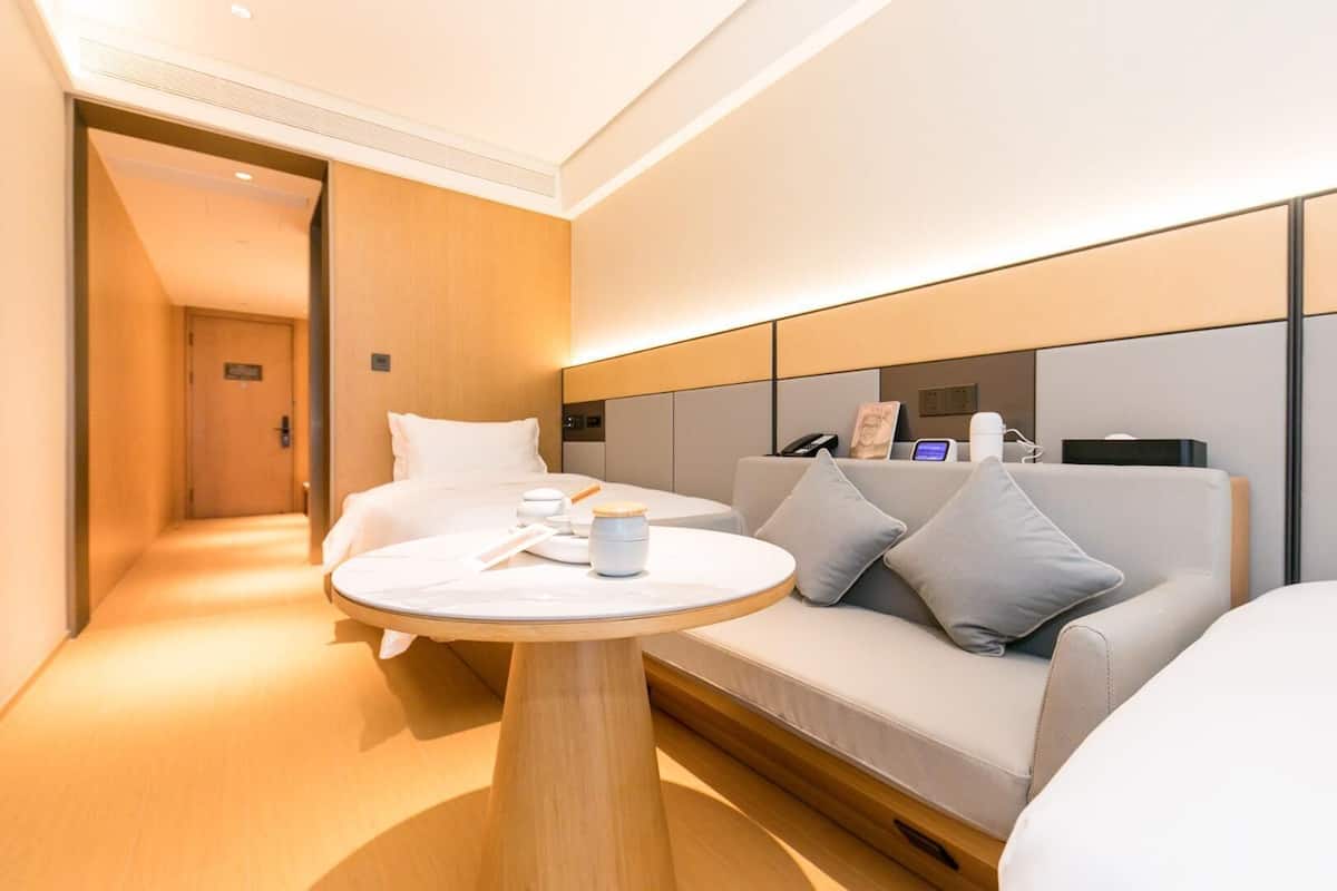 Ein Hotelzimmer mit einem Bett, einem Sofa, einem runden Tisch und einem Nachttisch mit einer Tasse.