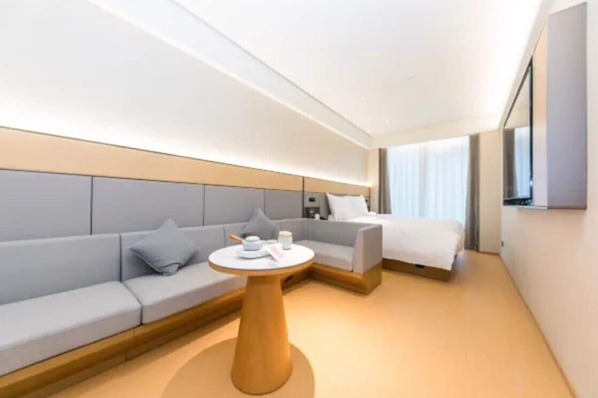 Ein modernes Hotelzimmer mit einer Couch, einem Bett, einem runden Holztisch und einem an der Wand befestigten Fernseher.