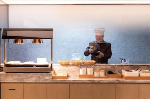 Uno chef prepara cibo dietro un banco da lavoro, con cesti, contenitori e utensili.