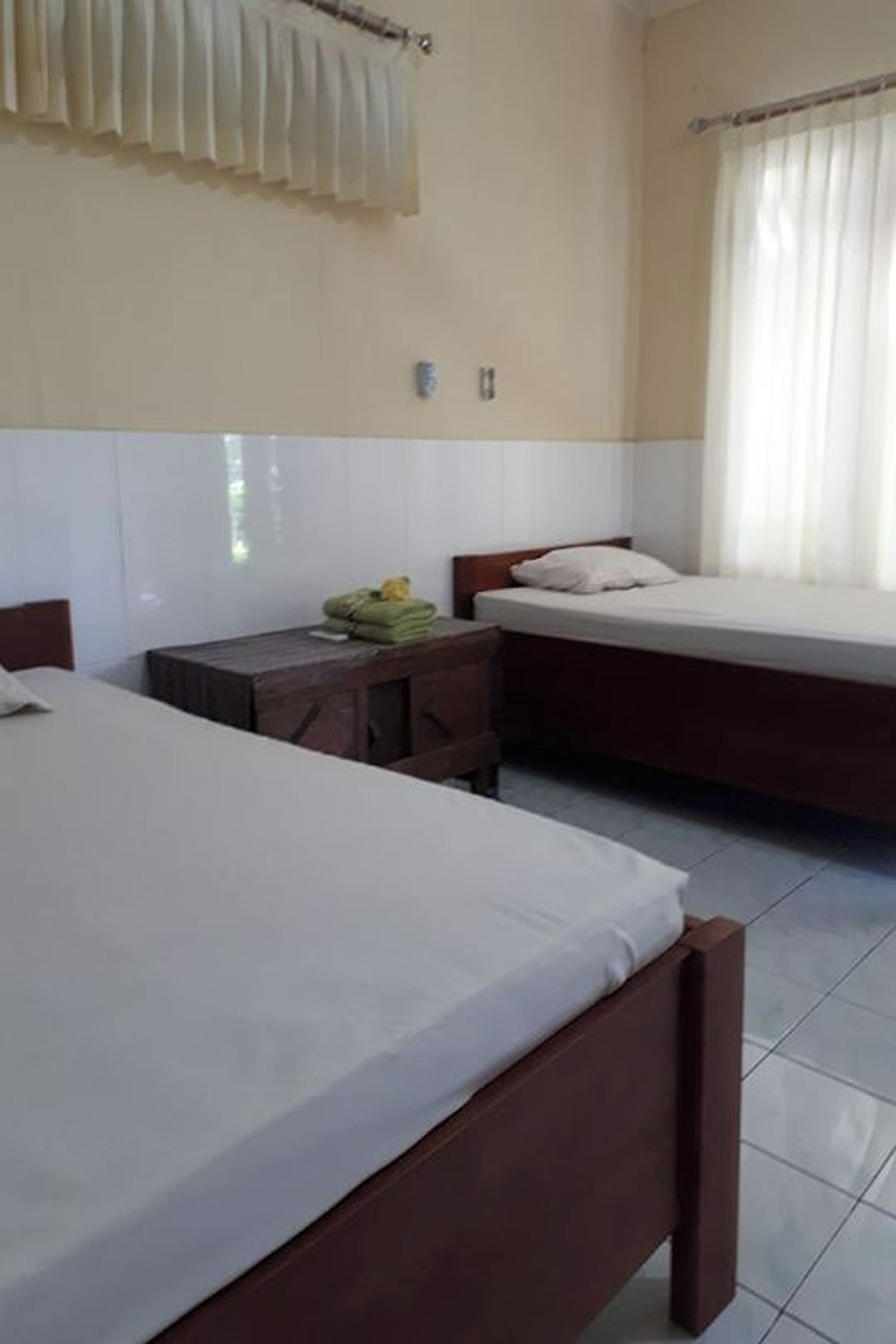 A hotel room with two beds, a small table with towels, and a window with curtains.