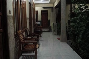 A corridor with wooden benches, a tiled floor, and a wall with greenery. - Sagita Bungalow by Zuzu (Gili Trawangan)