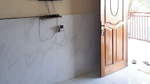 A room with a tiled floor, a mounted television, an air conditioning unit, a fan, and a wooden door. - Sagita Bungalow by Zuzu (Gili Trawangan)