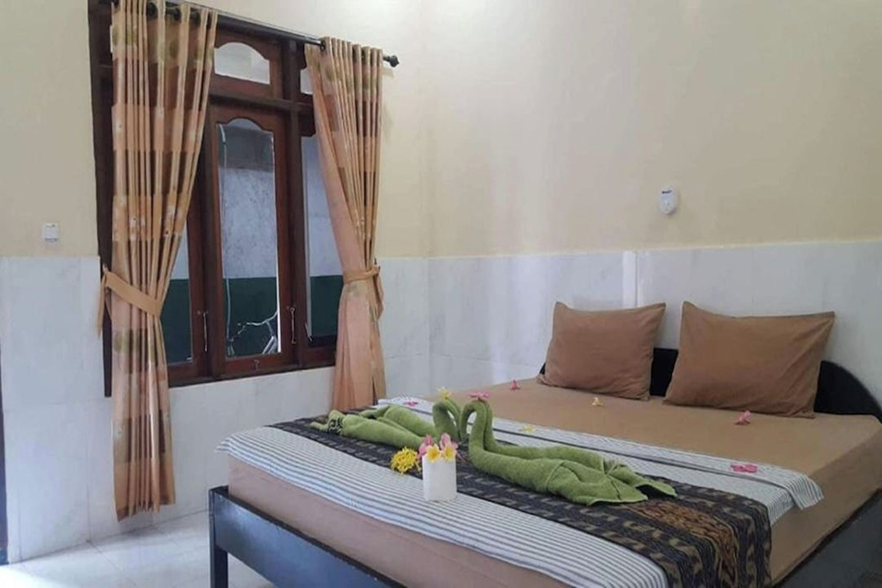 A room with a bed, a bench, a window with curtains, and a wall-mounted light.