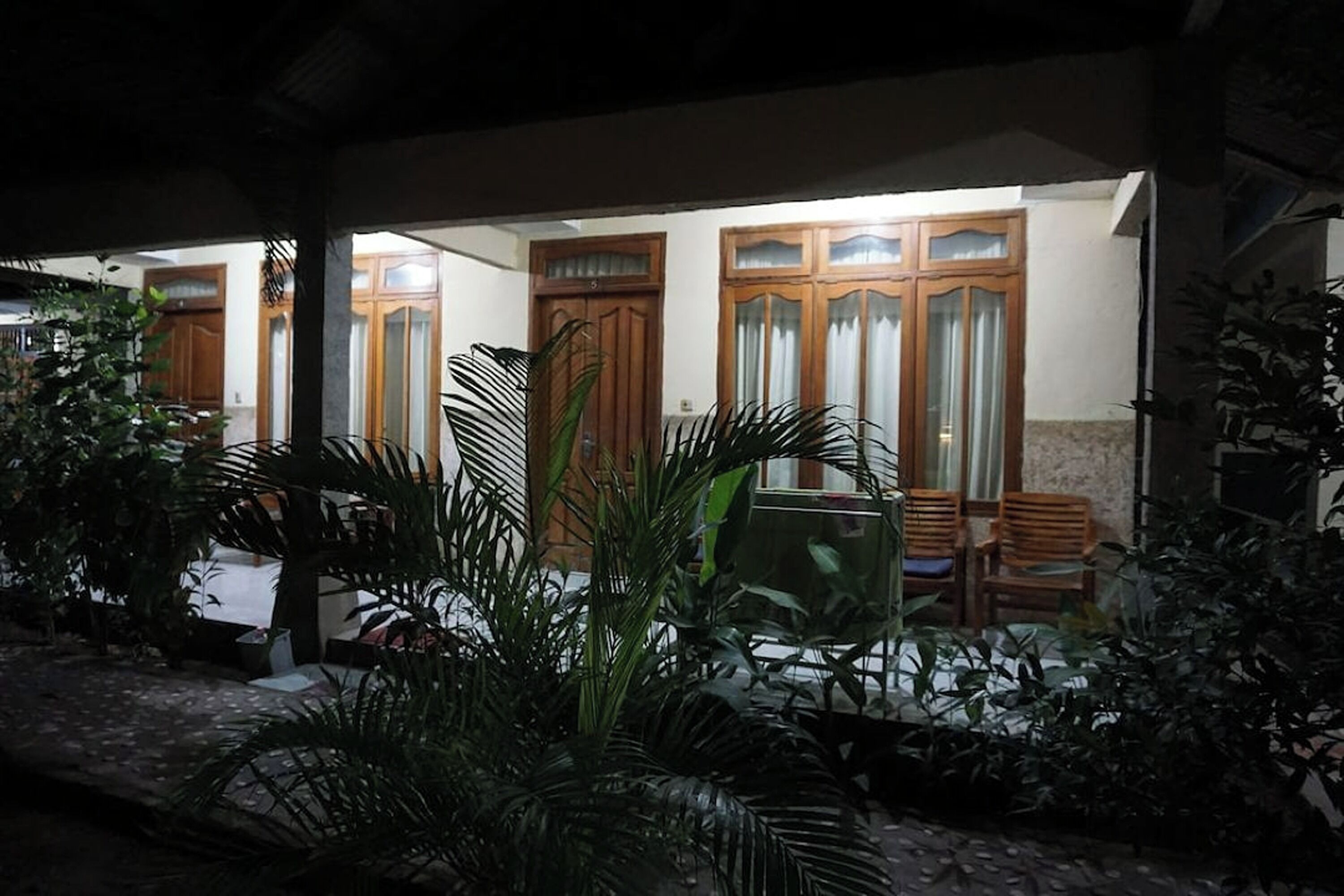 A covered outdoor area with wooden doors, potted plants, and a seating area.
