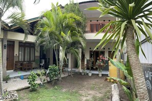 A courtyard with a palm tree, a bicycle, and a building with a balcony. - Sagita Bungalow by Zuzu (Gili Trawangan)