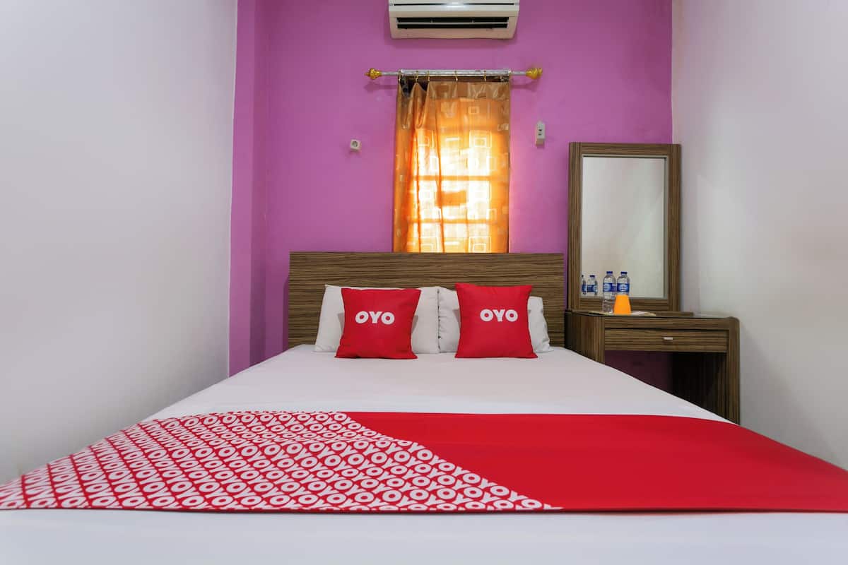 Una habitación de hotel con cama, mesita de noche, espejo y ventana con cortina.