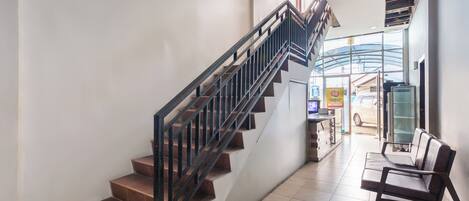A staircase with a metal railing leading to a second floor, a bench, and a reception area with a car visible outside.