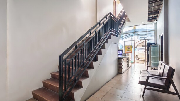 Una escalera con barandilla metálica que lleva a un segundo piso, un banco y una zona de recepción con un coche a la vista.
