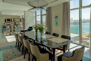 A modern dining area with a glass table, chairs, a bookshelf, and a view of the city and water. - Th8 Palm Dubai Beach Resort Vignette Collection (Dubai)