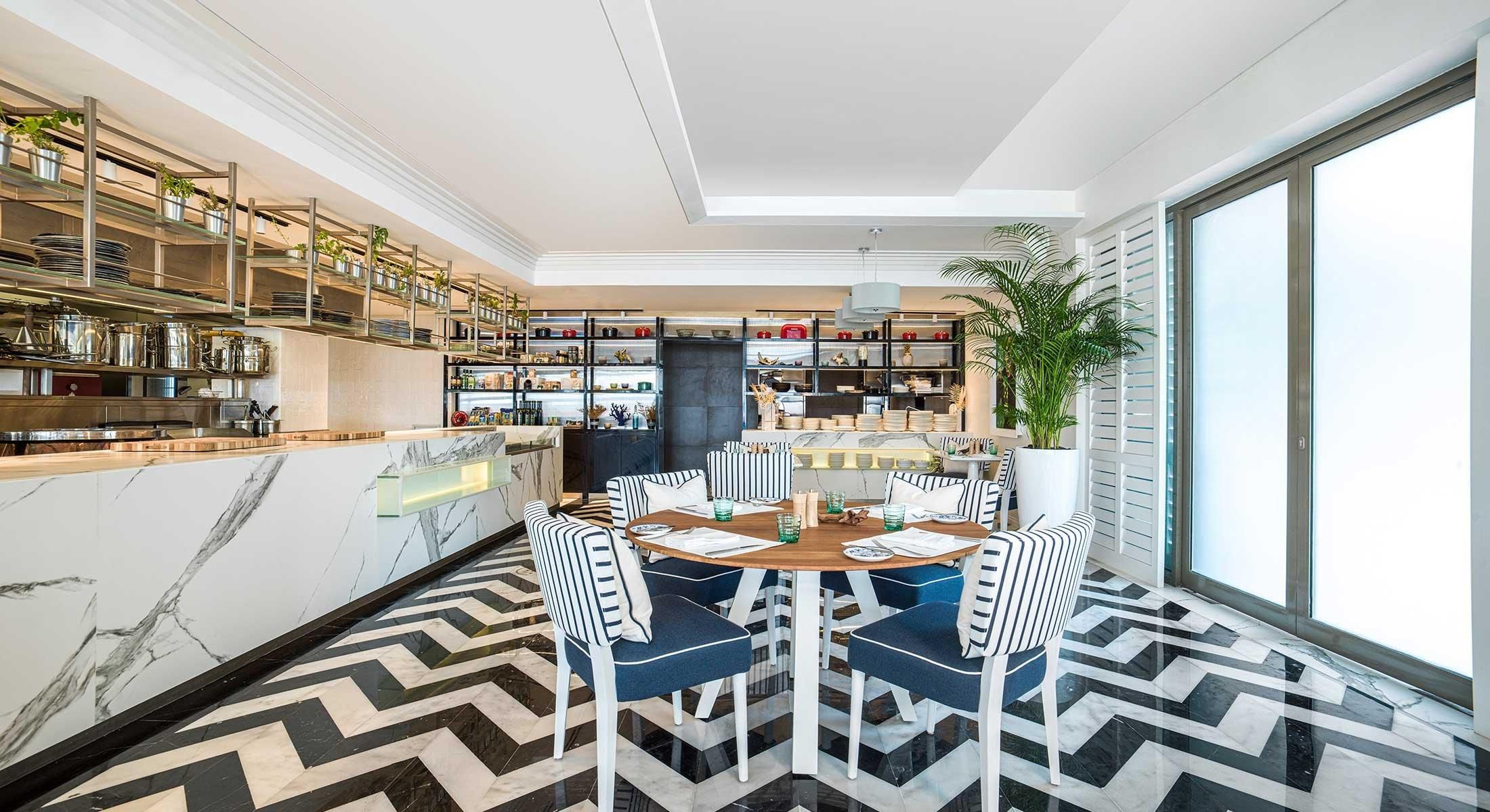 A modern kitchen with marble countertops, a dining area with striped chairs, and a large window.