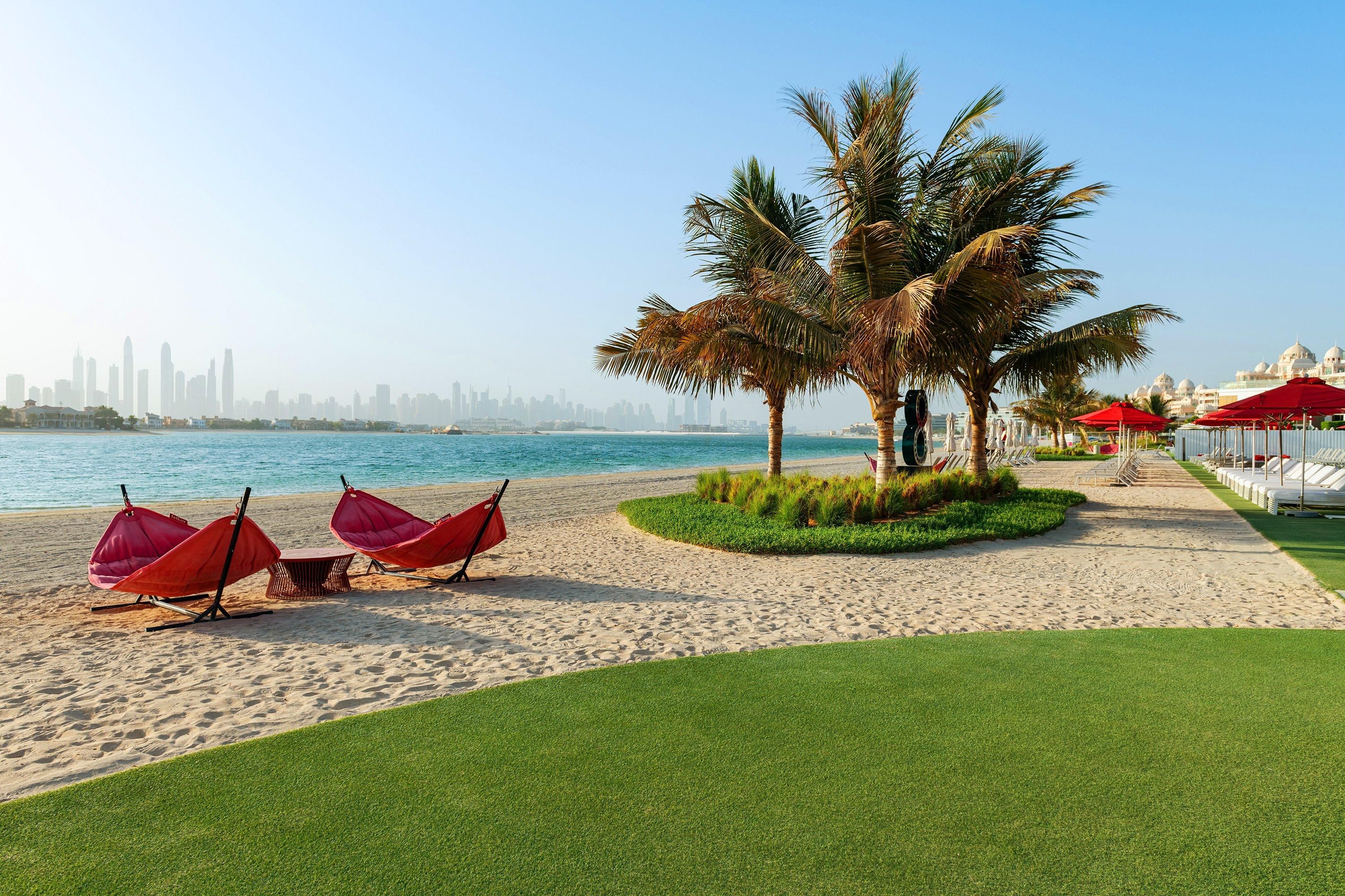 A beach with palm trees, a water view, and red umbrellas.