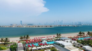 Un resort con zona de piscina, playa y el horizonte de una ciudad al fondo.