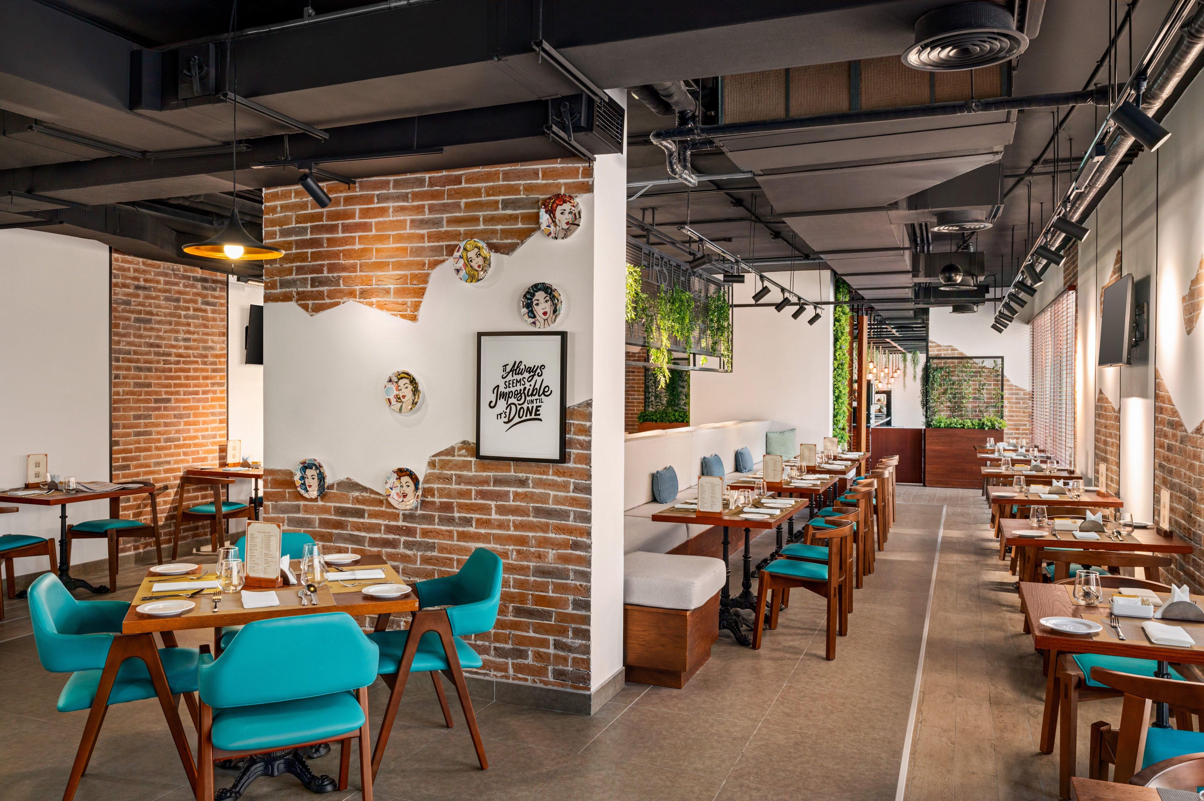 A restaurant with brick walls, wooden tables, teal chairs, and a menu stand.