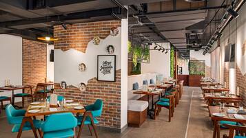A restaurant with brick walls, wooden tables, teal chairs, and a menu stand.