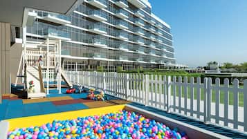 Een modern gebouw met balkons, een speelruimte voor kinderen met een bällebad en een witte hek.