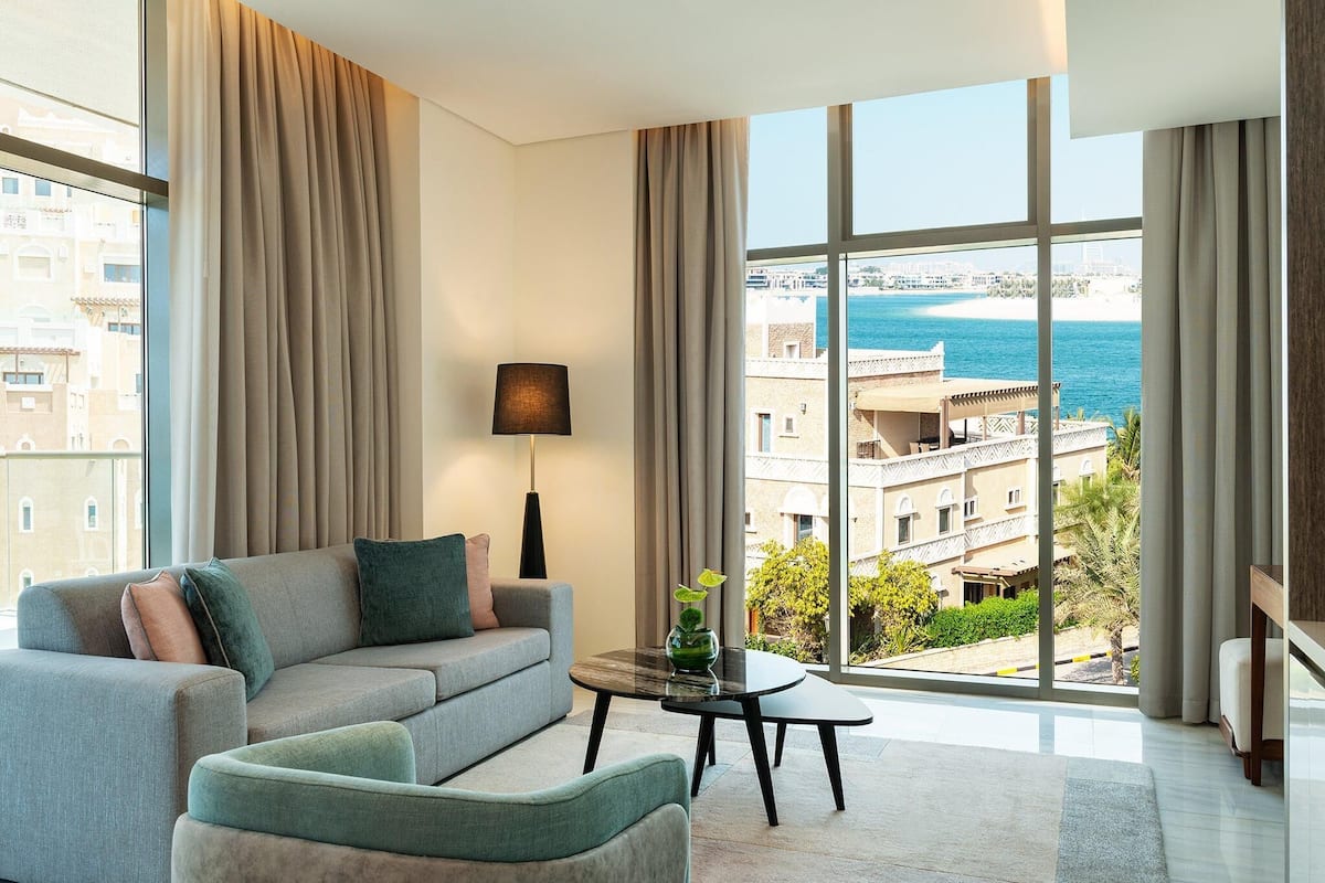 A modern living room with a sofa, a small table, and a view of the sea and buildings.