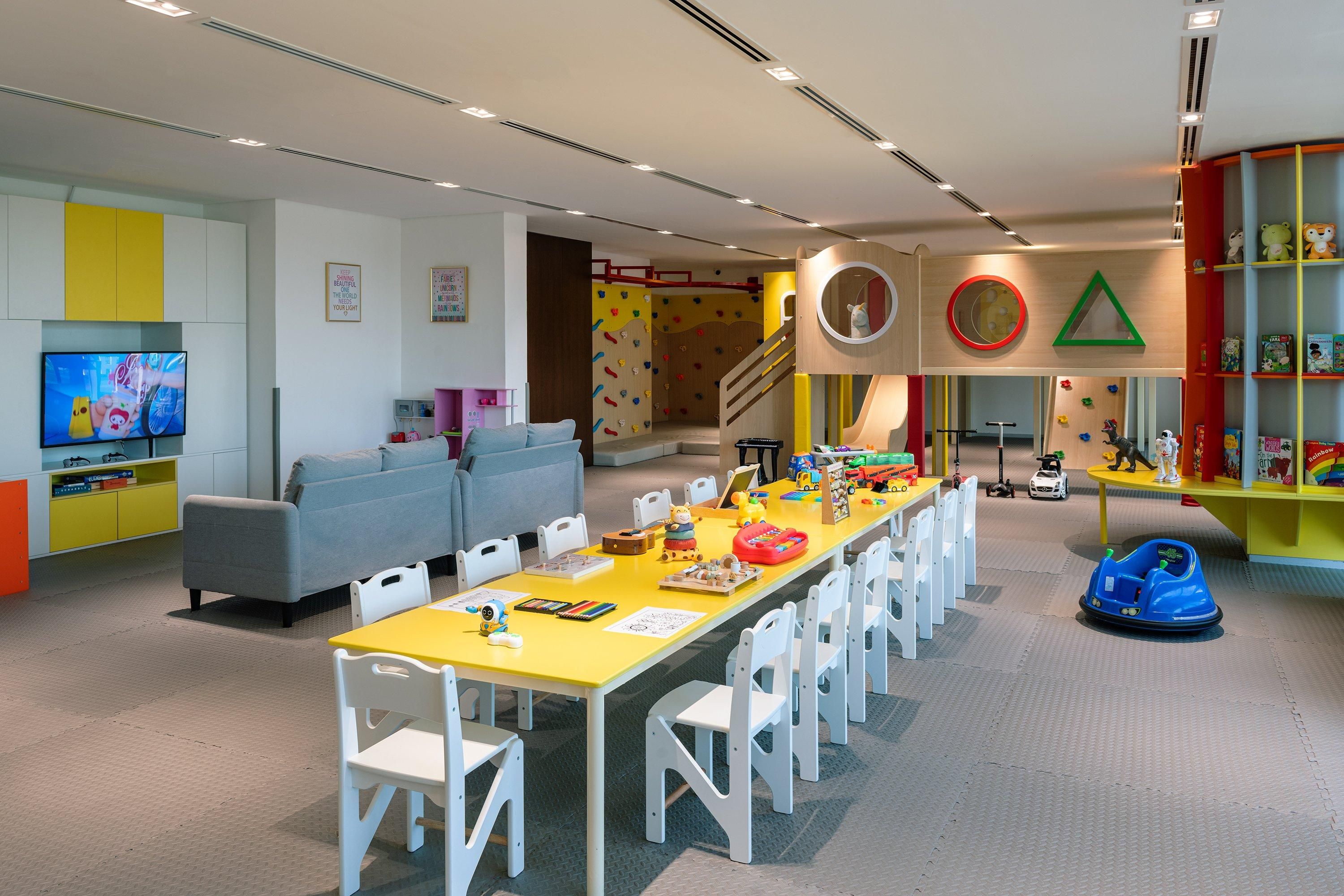 A children's play area with a climbing wall, a sofa, a dining table with chairs, and a television.