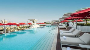 Una piscina en la azotea con sombrillas rojas, sillas de descanso y vistas del horizonte de la ciudad.