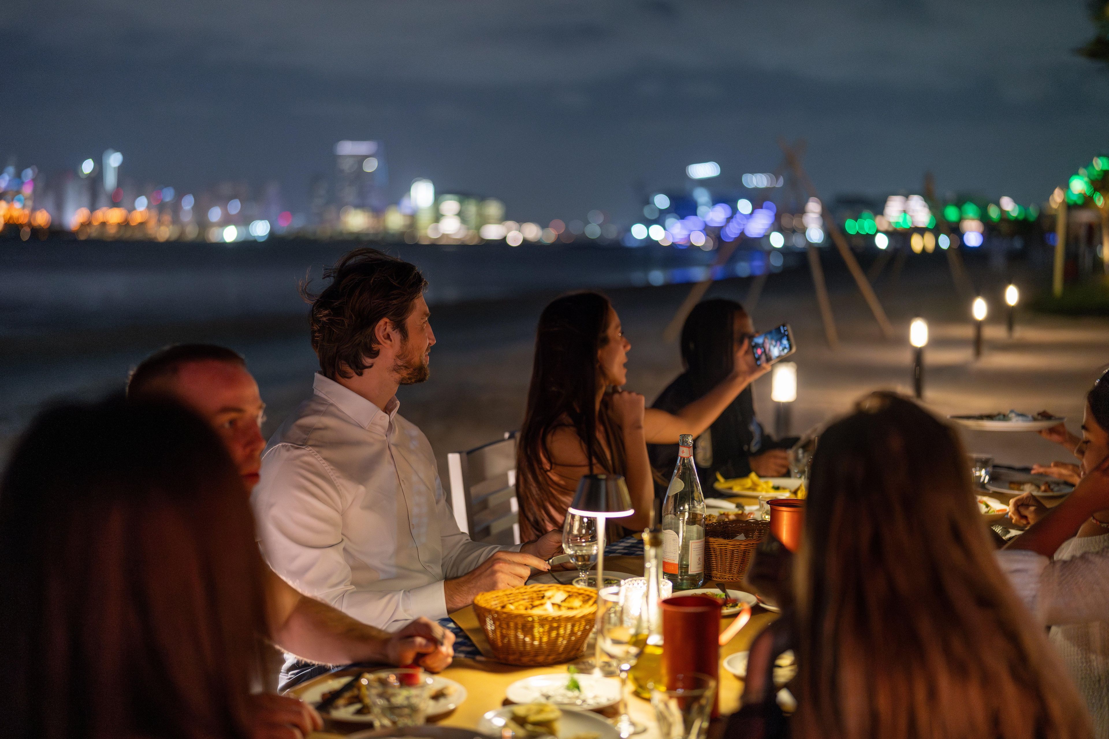 A group of people dining at an outdoor table with a city skyline in the background.