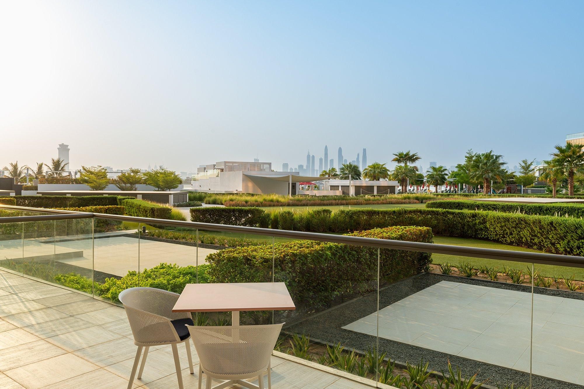 A rooftop terrace with a table and chairs, a view of the city skyline, and landscaped gardens.