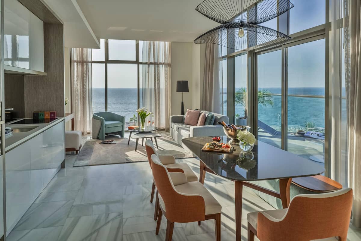 A modern kitchen with a dining area, large windows with ocean views, and a balcony with a view of the sea.