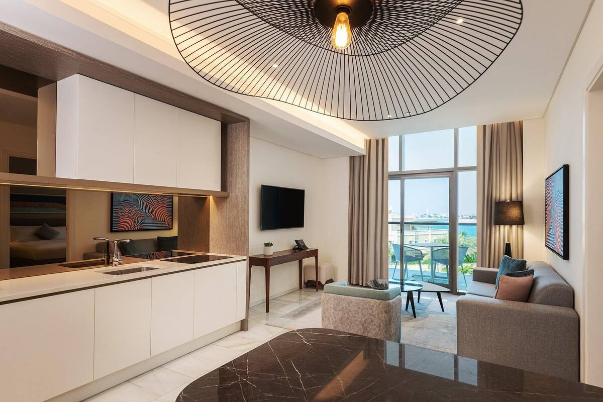 A modern kitchen with a marble island, a dining area with a black marble table, and a living area with a sofa and a TV.