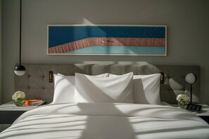 A neatly made bed with white linens, a headboard with a textured design, a framed artwork above the bed, and a bedside table with a vase of flowers and a book. - Th8 Palm Dubai Beach Resort Vignette Collection (Dubai)