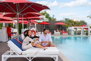 A poolside area with lounge chairs and red umbrellas. - Th8 Palm Dubai Beach Resort Vignette Collection (Dubai)