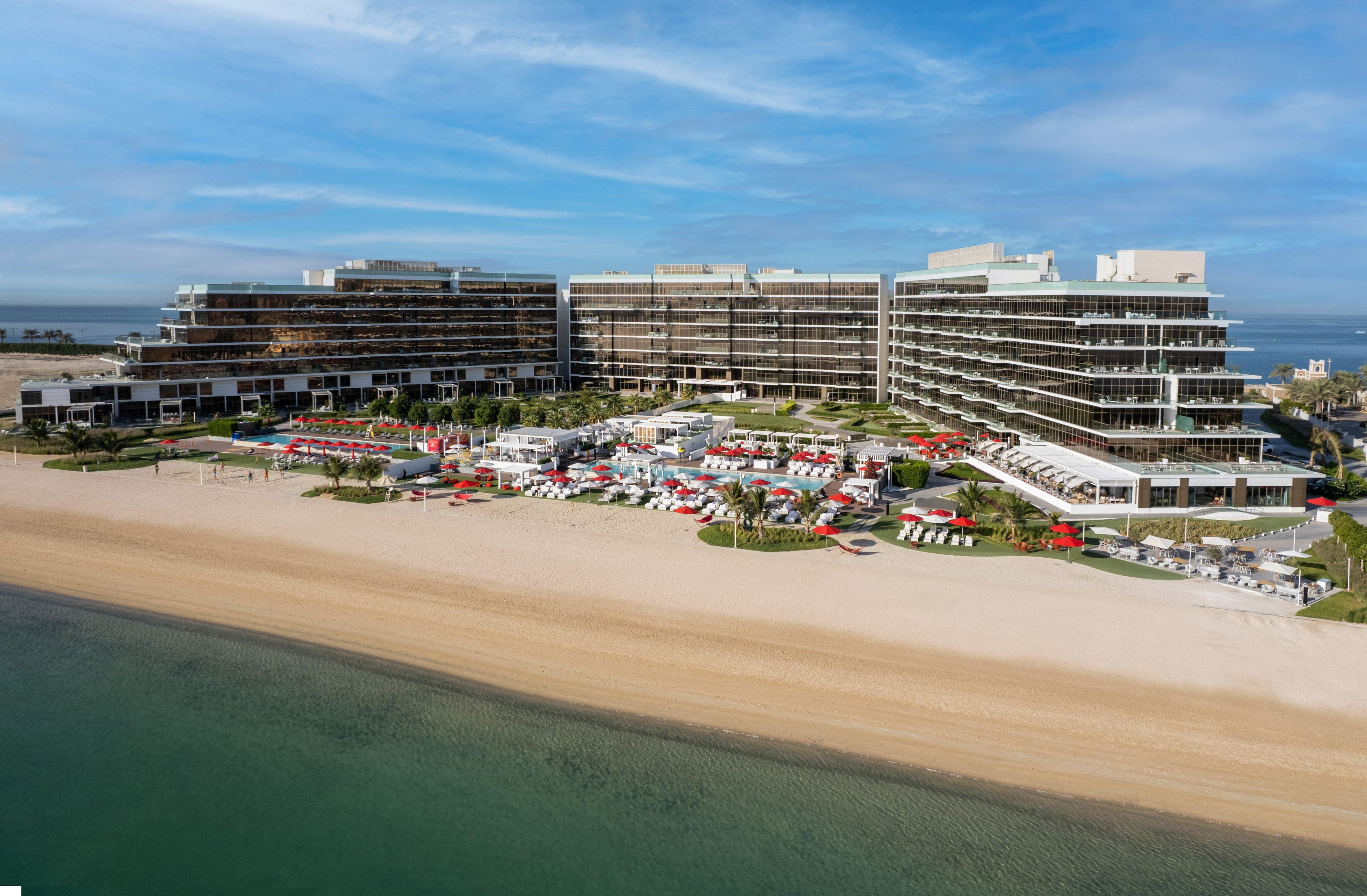 Een hotel aan het strand met meerdere verdiepingen, een zwembadgedeelte en uitzicht op het strand.