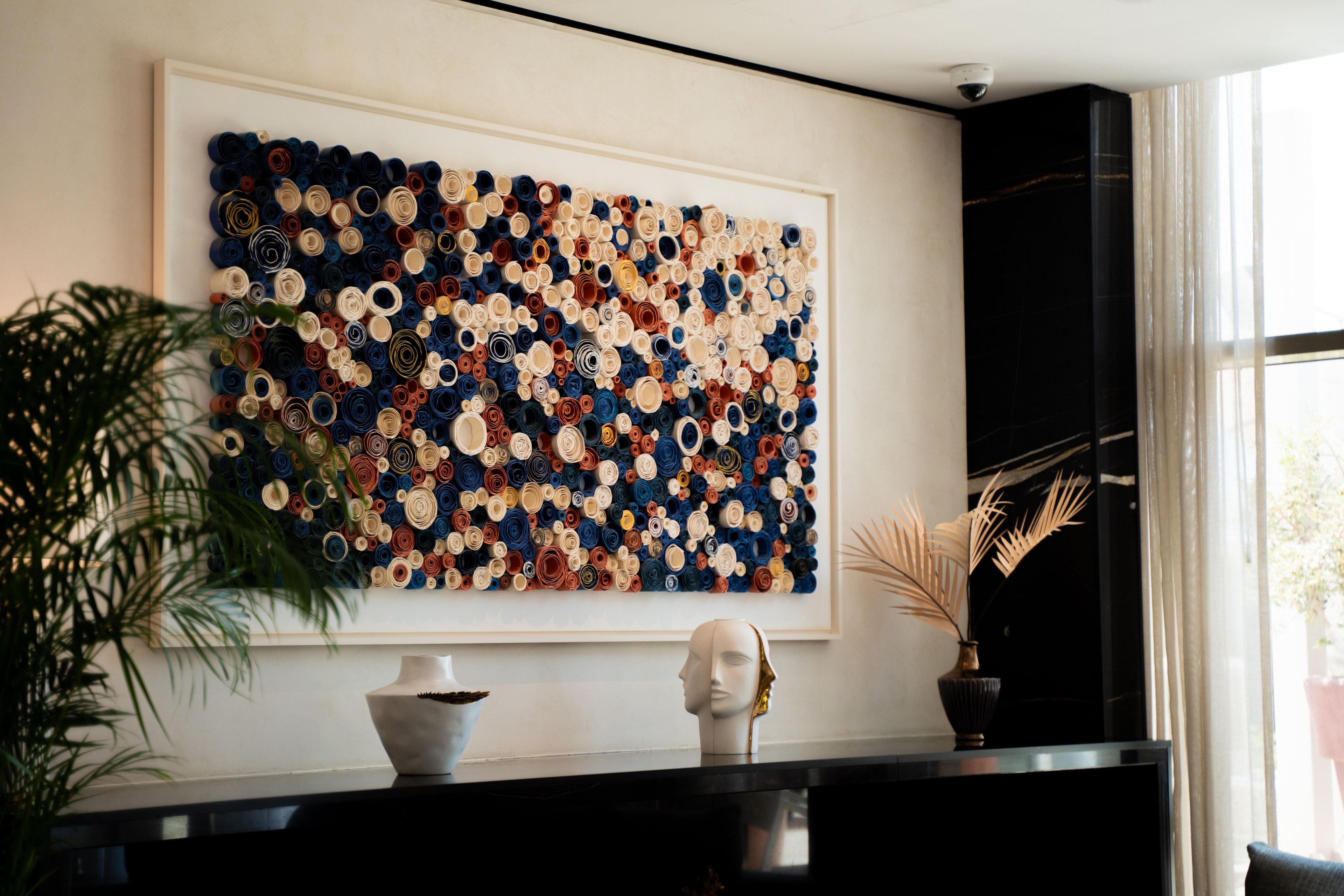 A room with a large abstract art piece on the wall, a black console table with a bust and a vase, and a potted plant.