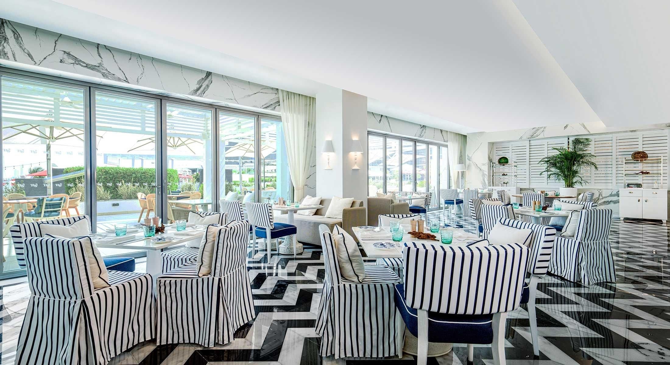 A modern hotel room with large windows, striped furniture, and a marble floor.