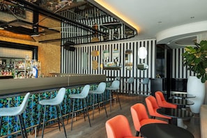 A bar area with a counter, bar stools, and seating with tables and chairs. - Th8 Palm Dubai Beach Resort Vignette Collection (Dubai)